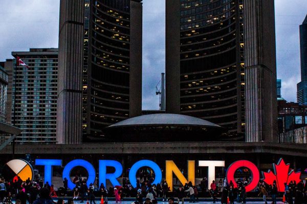 Toronto sign in front of buildings downtown at dusk with people outside Toronto sign in front of buildings downtown at dusk with people outside